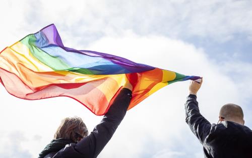 Två personer håller upp regnbågsflaggan mot himlen.