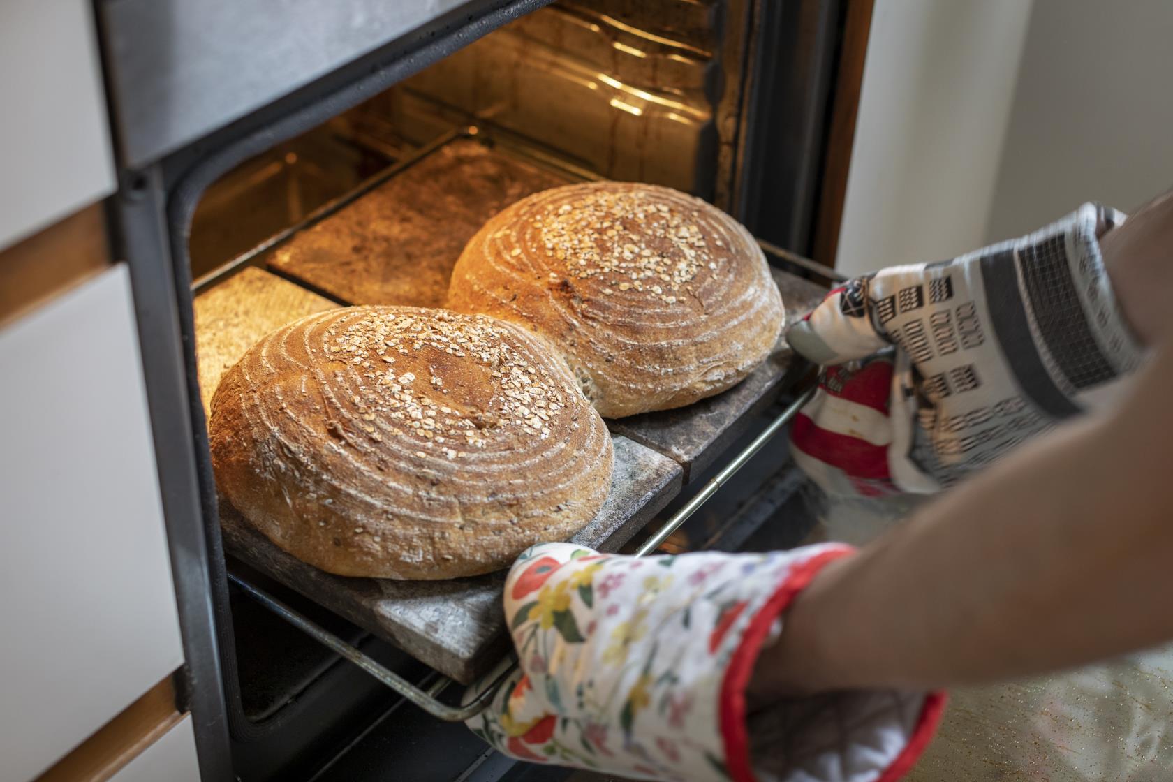 En person med ugnsvantar tar ut en plåt med två nybakta bröd ur ugnen.