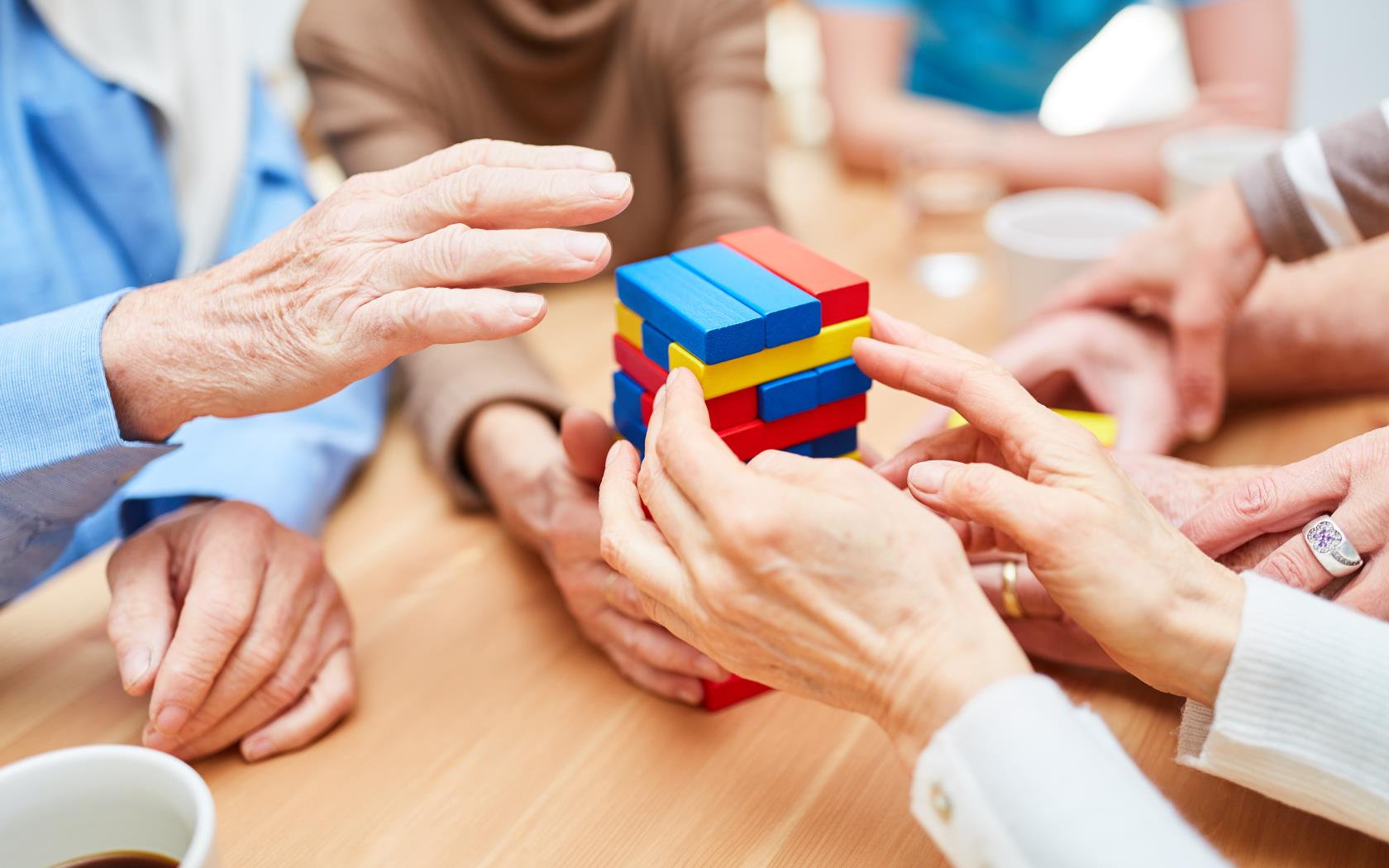 Några äldre sitter runt ett bord och spelar ett sällskapsspel med olikfärgade byggklossar som inte ska rasa.