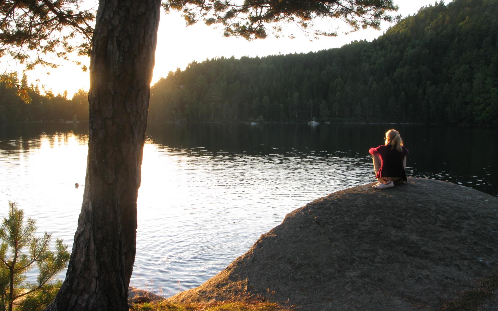 En kvinna sitter på en klippa och tittar på solnedgången.