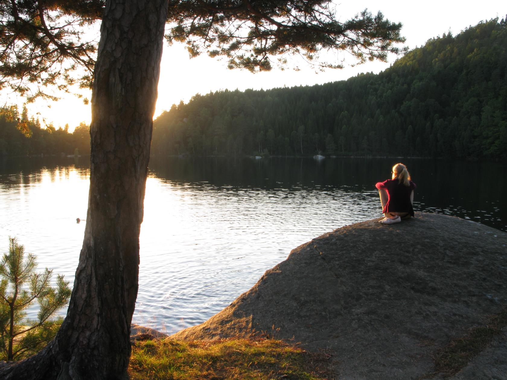 En kvinna sitter på en klippa och tittar på solnedgången.