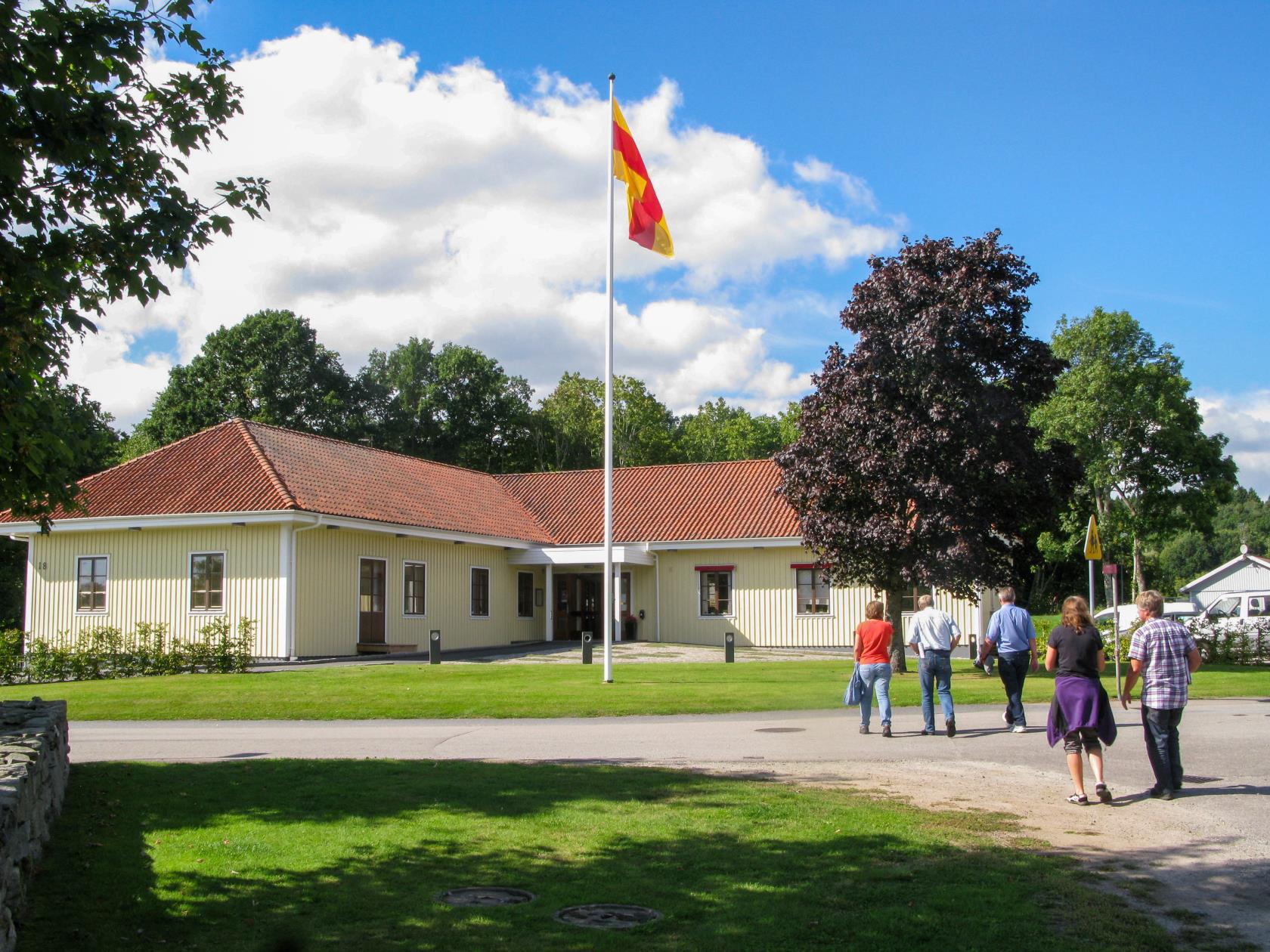 Några människor är på väg mot ett församlingshem med Svenska kyrkans flagga hissad.