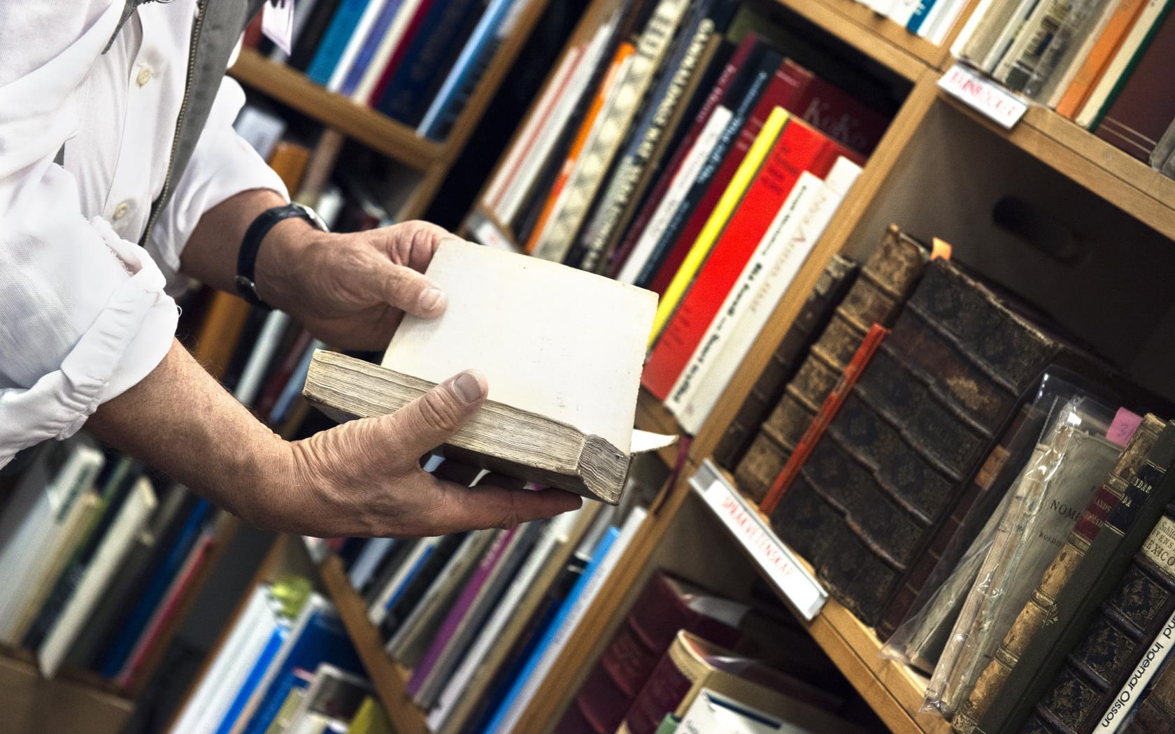 Någon bläddrar i en gammal bok från en bokhylla i ett bibliotek.