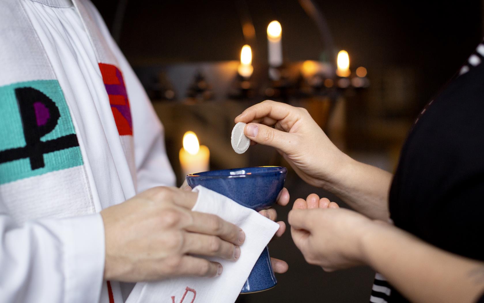 En präst håller fram nattvardskalken och en person doppar sin oblat.