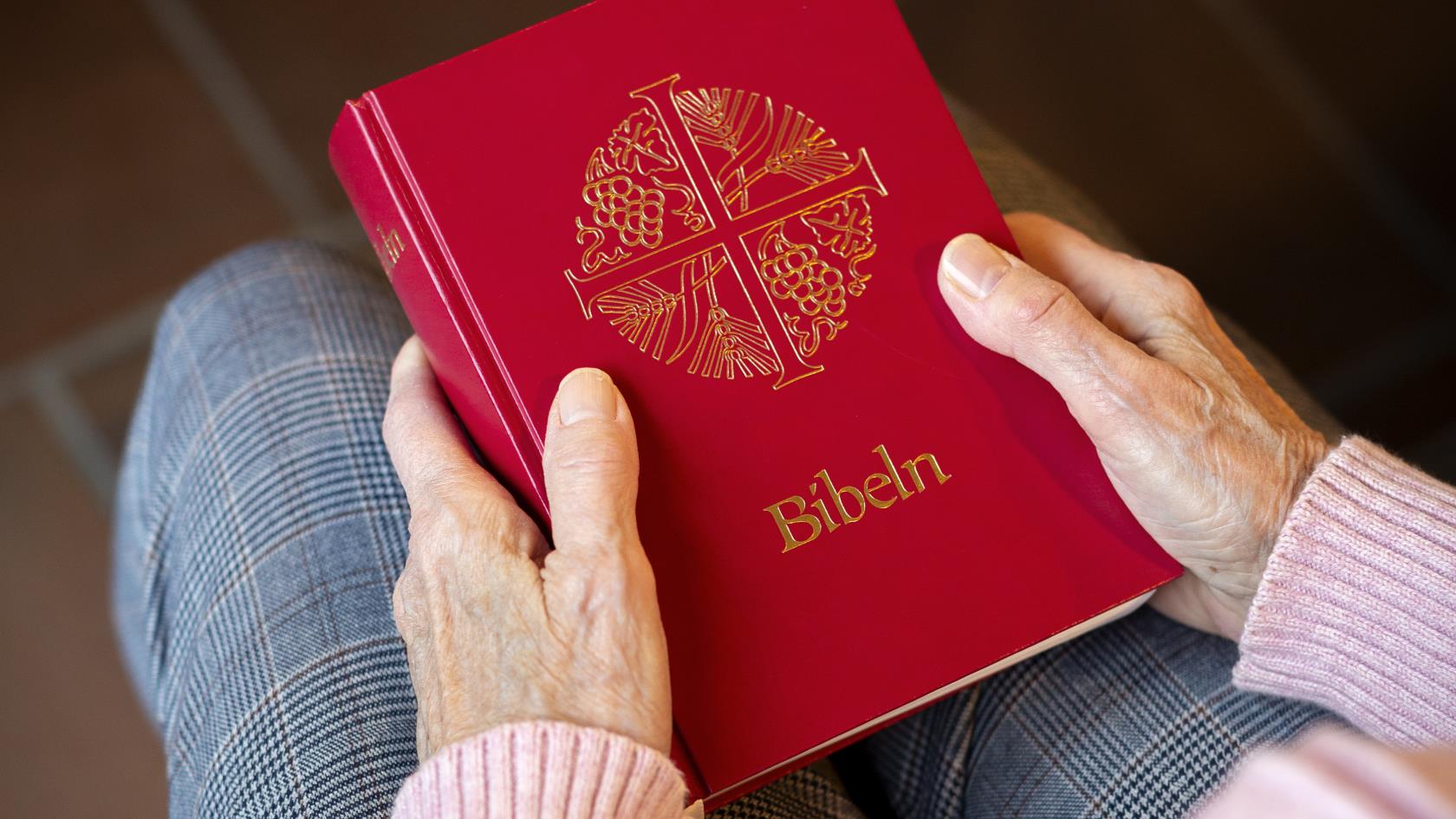 En person sitter i en kyrkbänk med en bibel i knät.