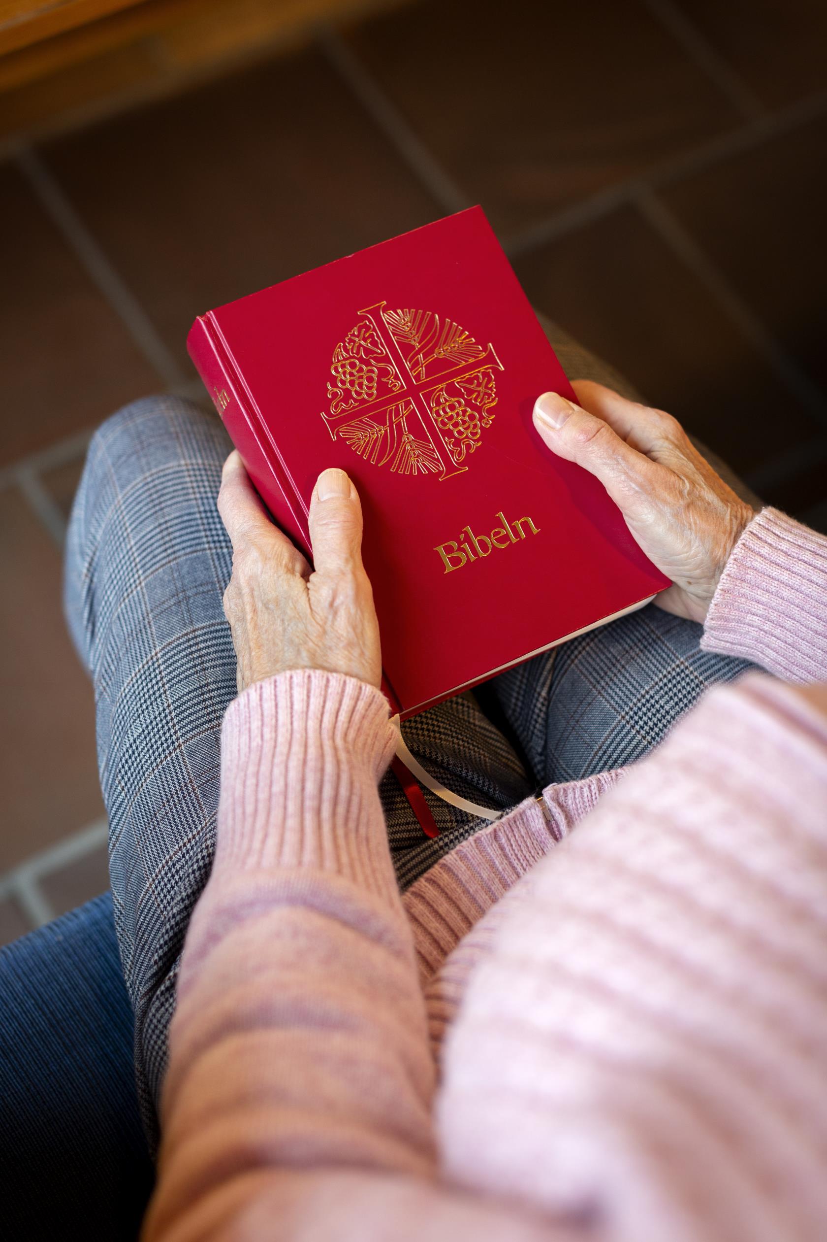 En person sitter i en kyrkbänk med en bibel i knät.