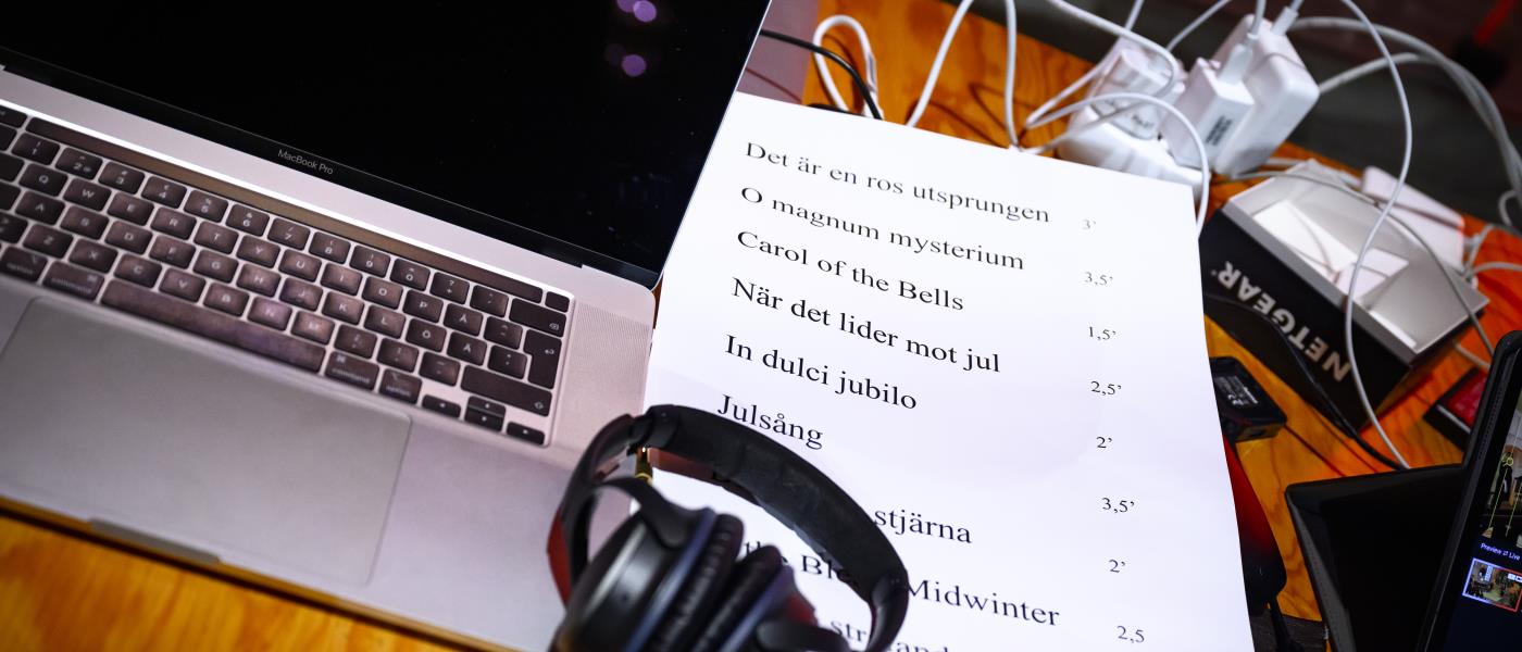 På ett skrivbord står en dator med hörlurar och en lista med julsånger på ett papper.