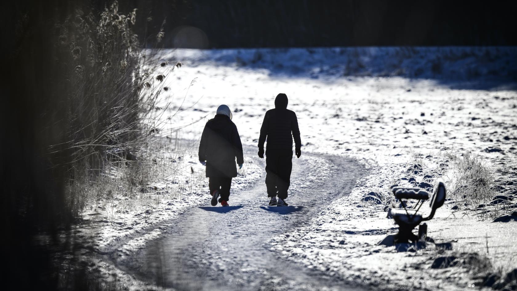 Två personer är ute på långpromenad. Det är vinter och solen skiner.