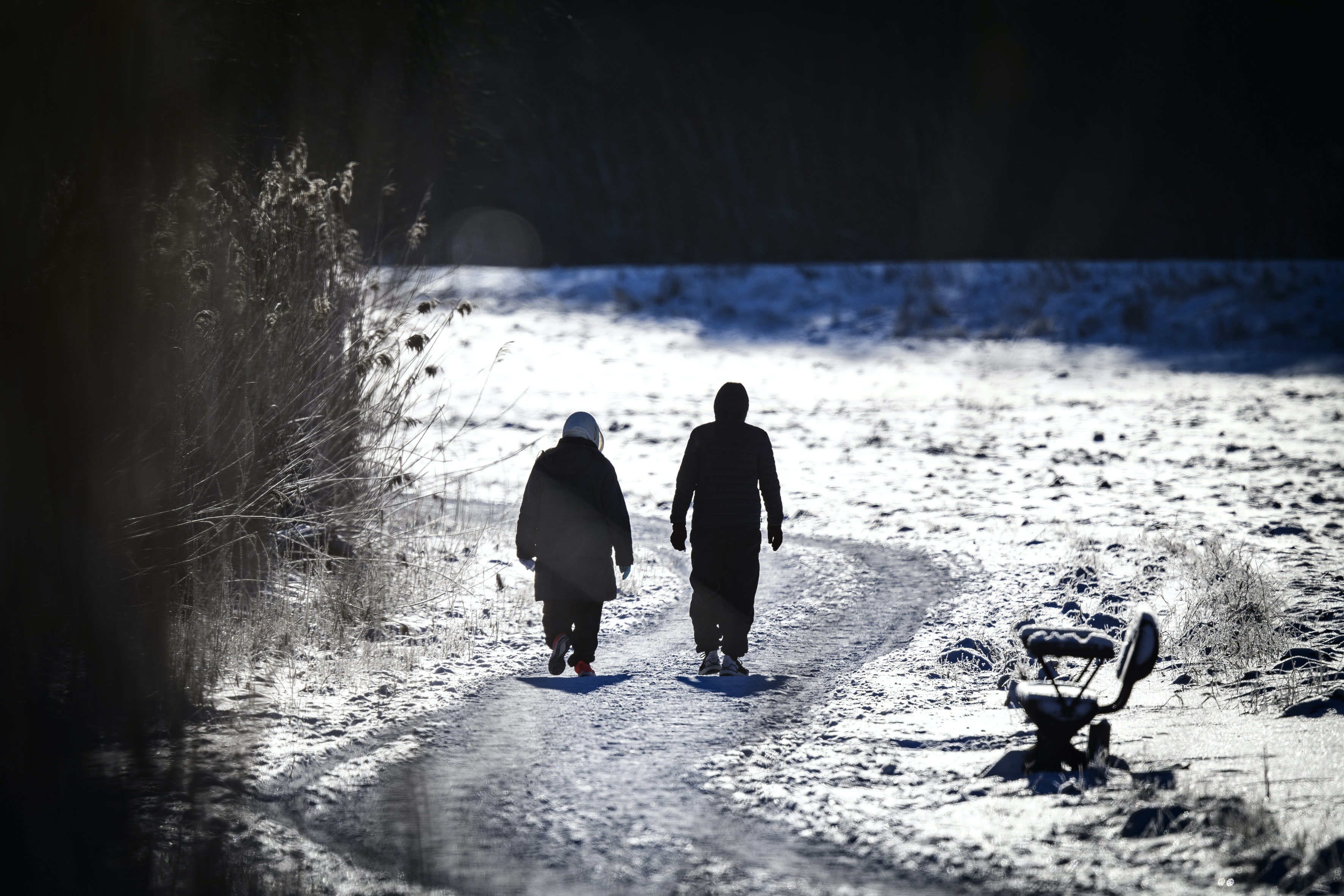 Två personer är ute på långpromenad. Det är vinter och solen skiner.