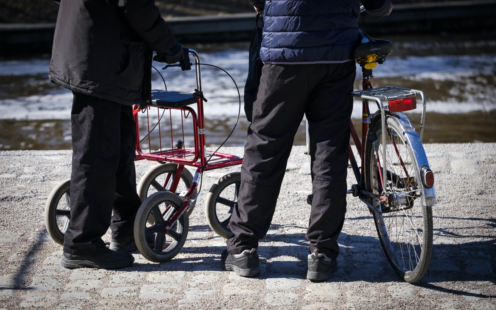 En person med rullator och en annan med cykel står tillsammans utomhus.