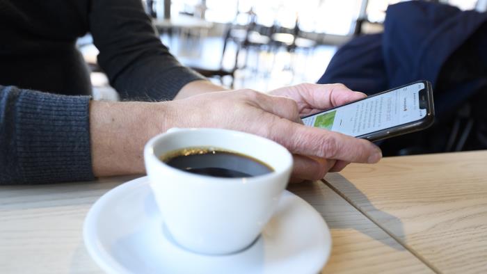 En person sitter med sin mobiltelefon och dricker kaffe.