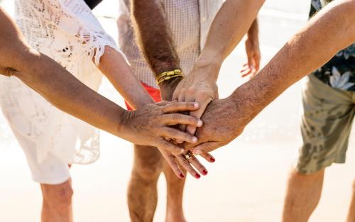 En grupp äldre personer står i en ring och lägger i sina händer på varandras.