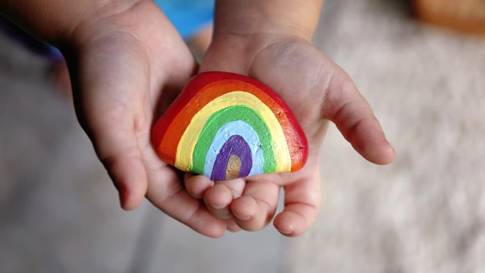 Ett barn håller upp en sten målad som en regnbåge.
