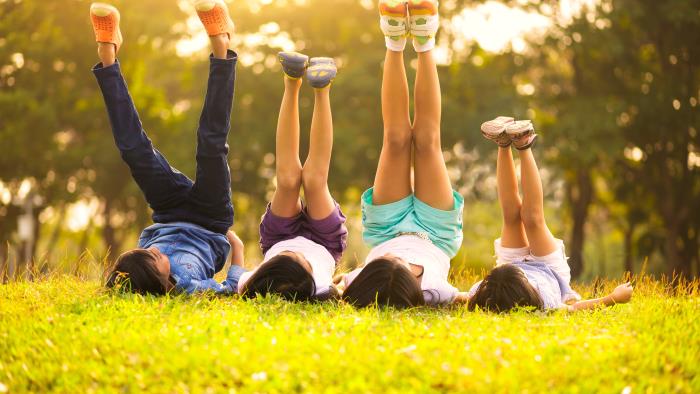 Fyra barn ligger i gräset på rygg och sträcker upp benen mot himlen.