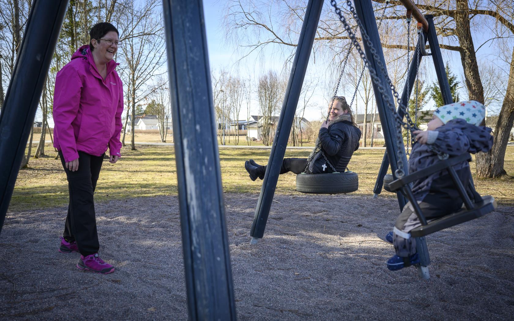 Två föräldrar gungar med sin bebis i en lekpark.