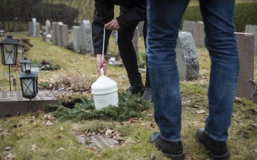Någon sänker ner en vit urna i marken på en gravplats.