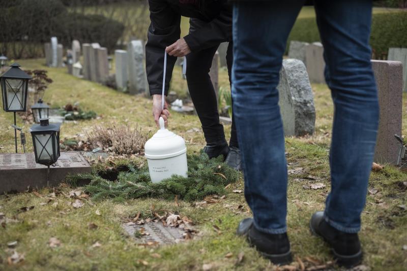 Någon sänker ner en vit urna i marken på en gravplats.