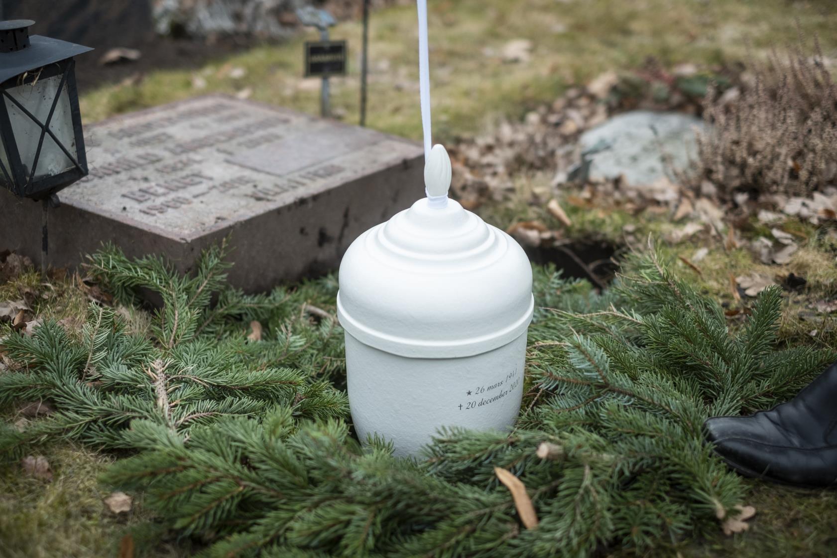 En vit urna sänks ner i marken på en gravplats.