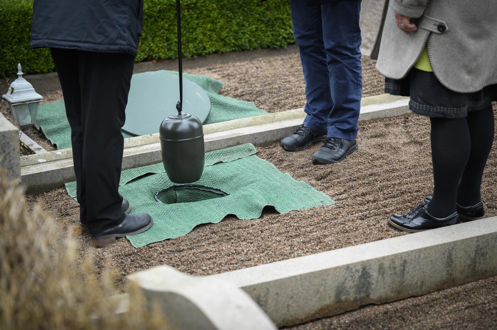 Någon sänker ner en urna i marken på en gravplats.