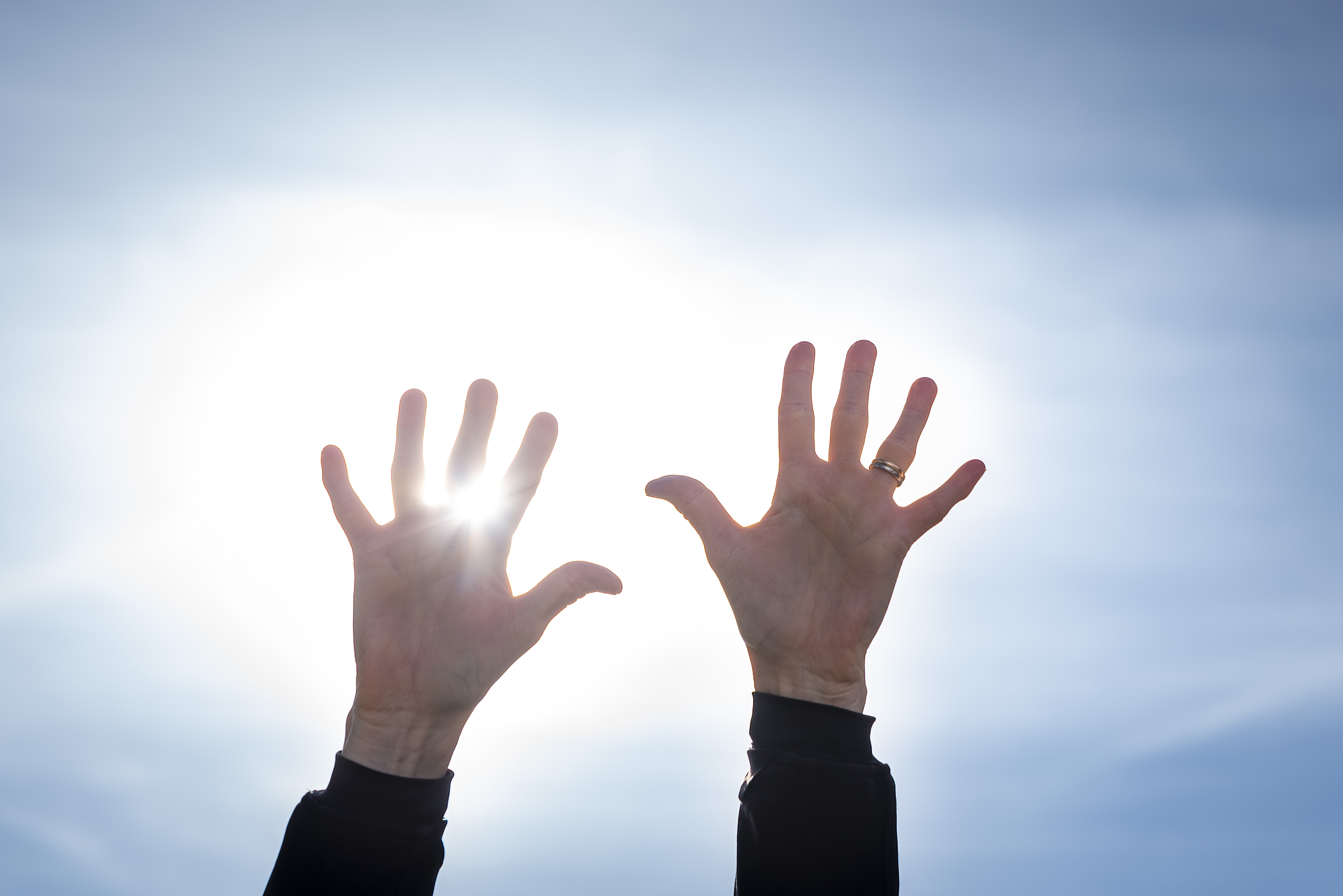 Två händer uppsträckta mot en blå himmel. Solen lysen mellan fingrarna.