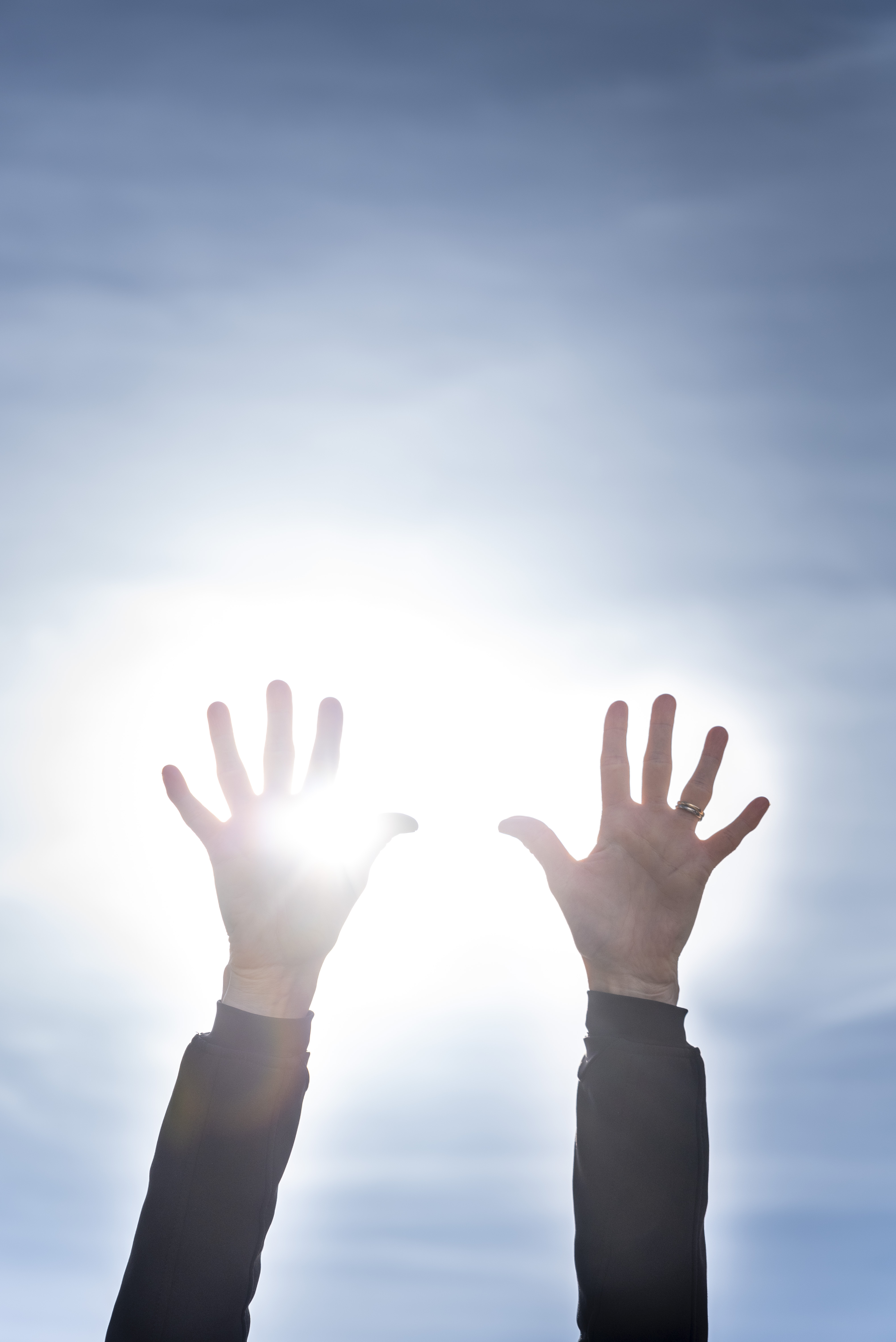 Två händer uppsträckta mot en blå himmel. Solen lysen mellan fingrarna.