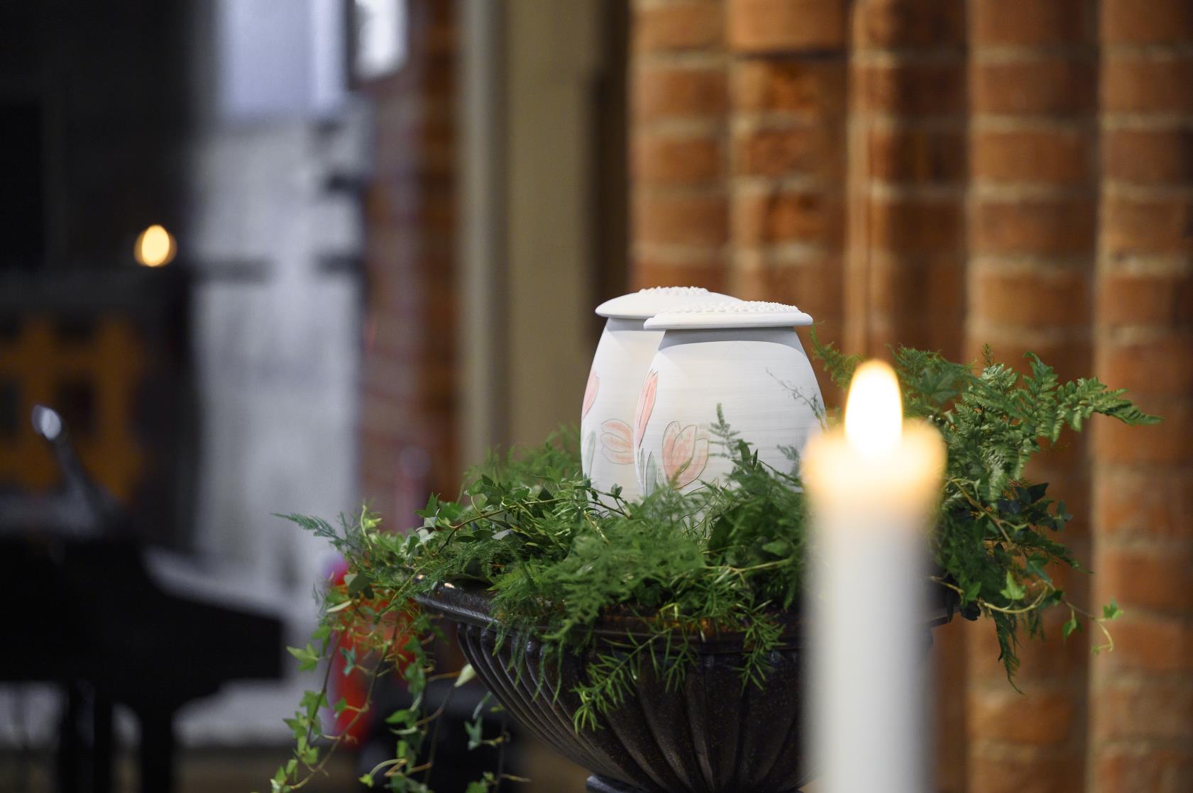 Två urnor med handmålade tulpaner står bland ormbunksblad på ett bord i kyrkan. Ett tänt ljus i förgrunden.