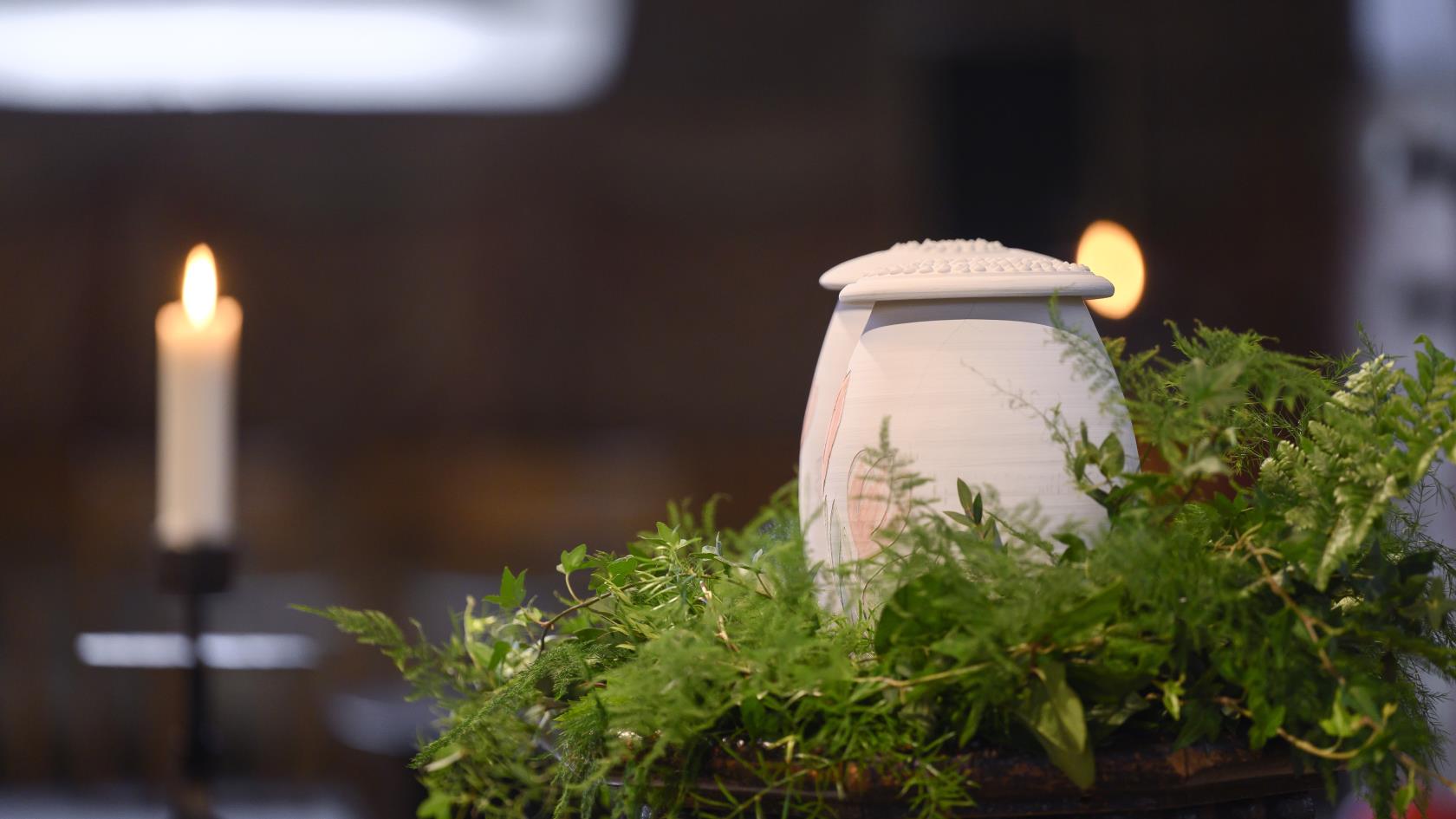 Två urnor står bland ormbunksblad på ett bord i kyrkan.