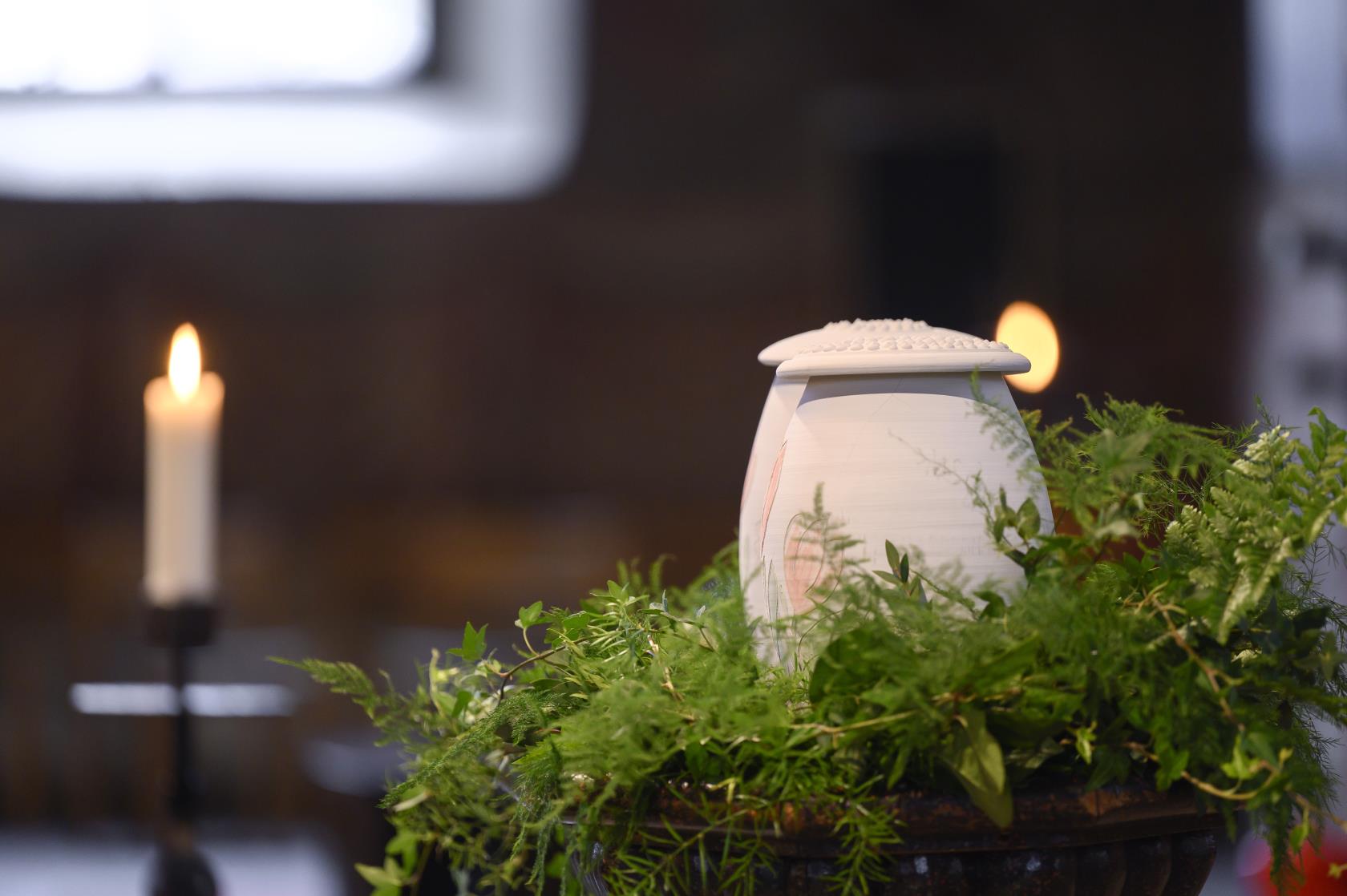 Två urnor står bland ormbunksblad på ett bord i kyrkan.