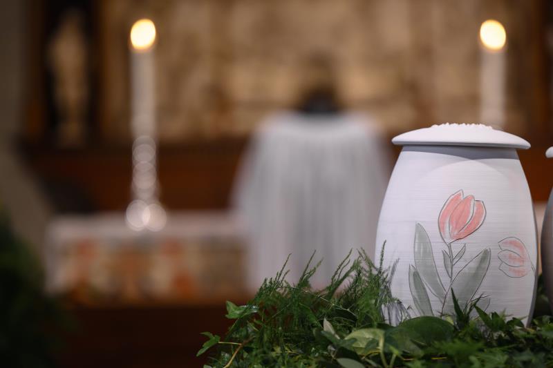 En urna med handmålade tulpaner står bland ormbunksblad på ett bord i kyrkan. En präst syns längre bort.