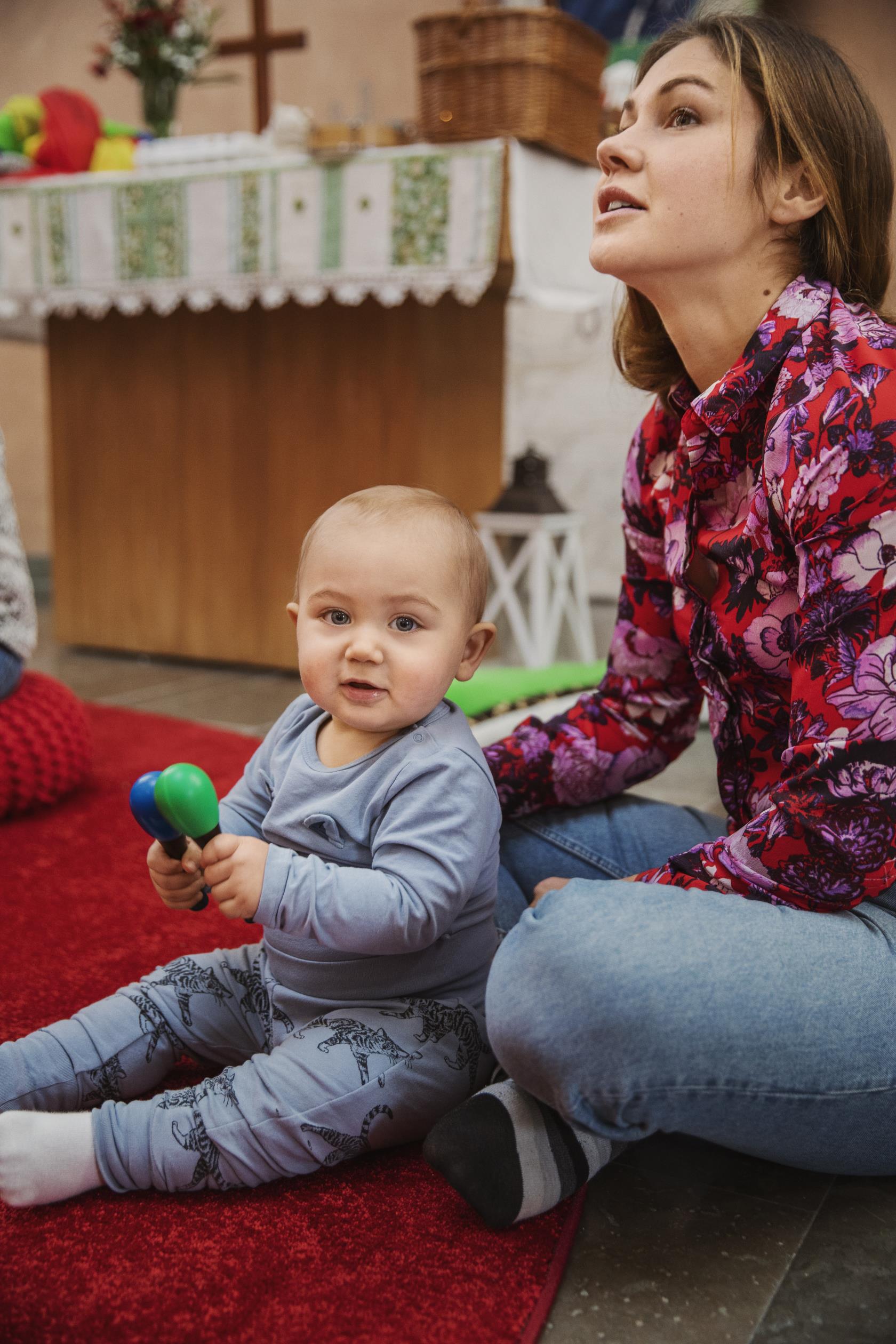 En bebis sitter på golvet framför sin mamma och spelar maraccas.