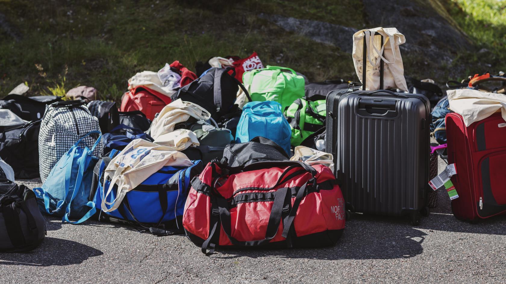 En samling packade resväskor och sportbagar står samlade utomhus.