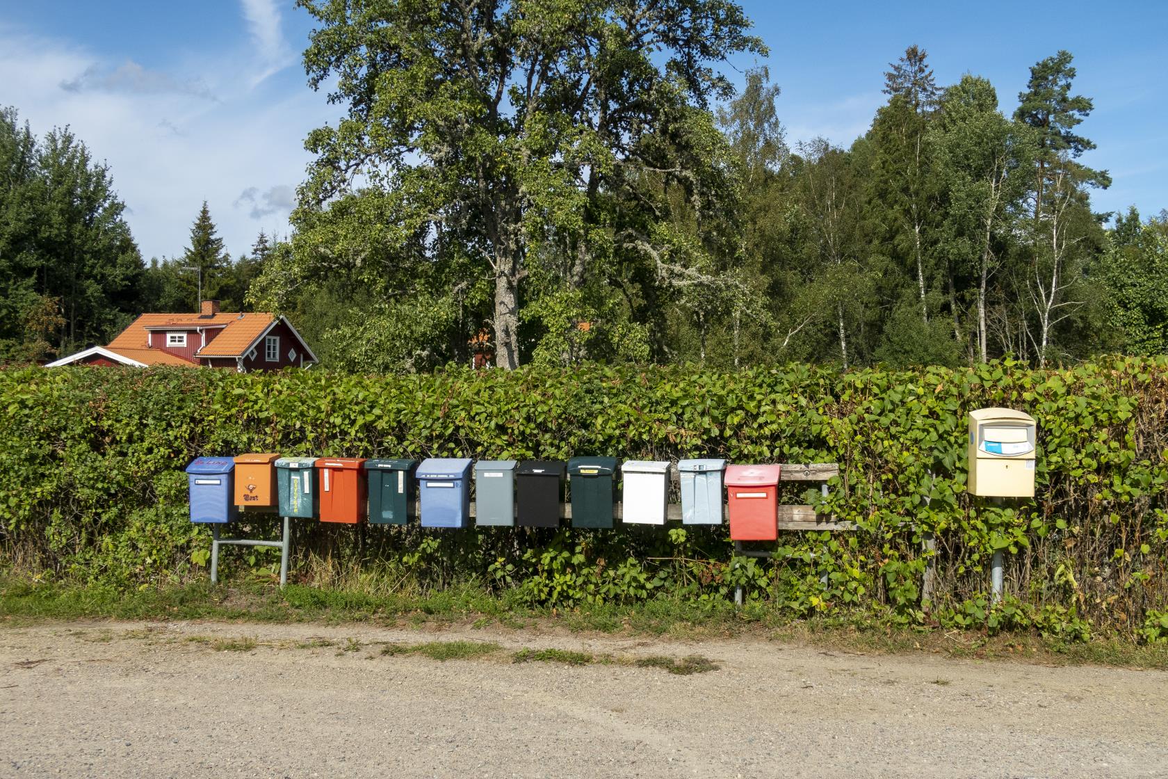 En rad med brevlådor vid en häck. En villa i bakgrunden.