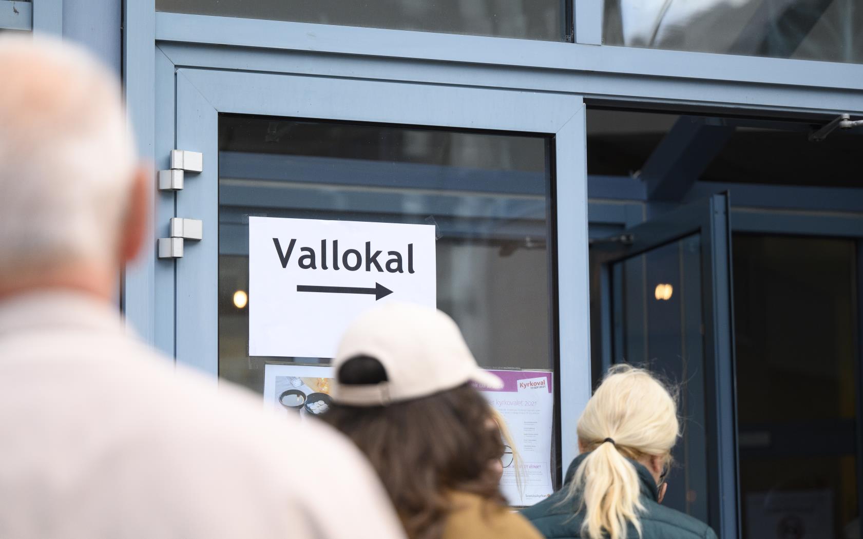 Människor som köar utanför en kyrka. Vid den öppna dörren sitter en lapp med texten Vallokal.