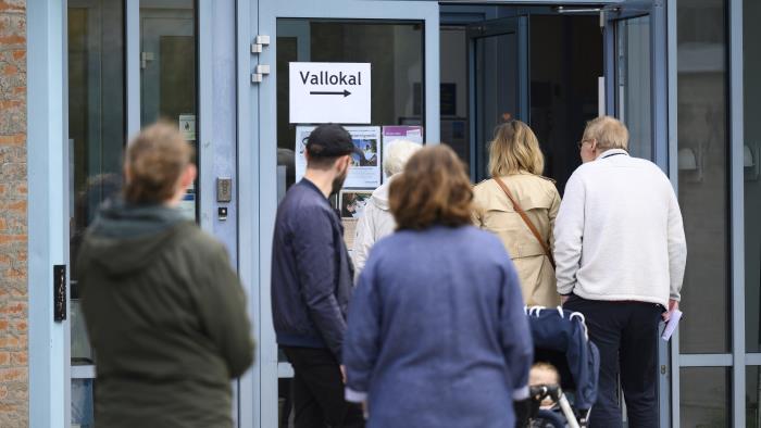 Människor som köar utanför en kyrka. Vid den öppna dörren sitter en lapp med texten Vallokal.