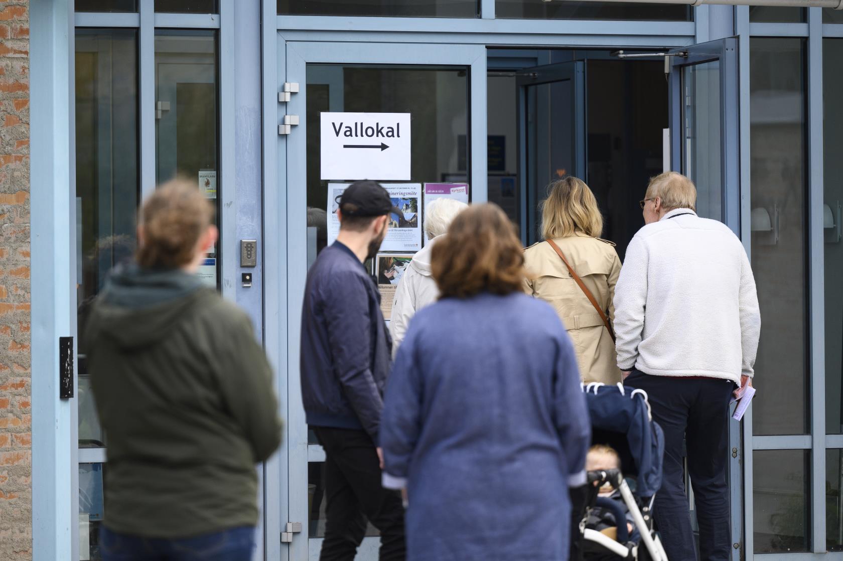 Människor som köar utanför en kyrka. Vid den öppna dörren sitter en lapp med texten Vallokal.