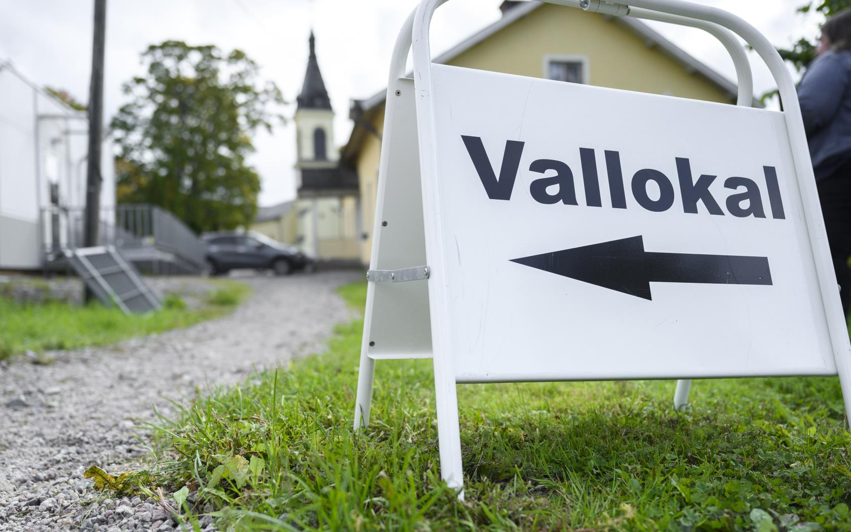 En skylt med texten Vallokal står i gräset utomhus. En kyrka syns otydligt i bakgrunden.