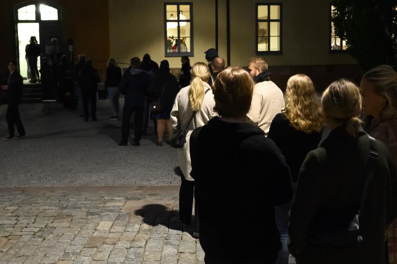 Människor som står i en lång kö utanför en byggnad i mörkret.