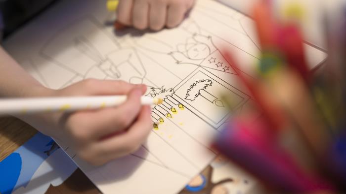 Närbild på ett barn som sitter och färglägger i en målarbok med jultema.