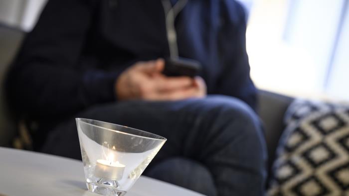 Ett värmeljus brinner på ett bord. I en soffa i bakgrunden syns en präst sitta med en mobiltelefon i handen.