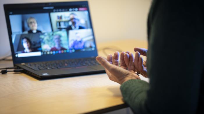 En person sitter vid ett skrivbord och har ett digitalt möte i datorn med några andra.