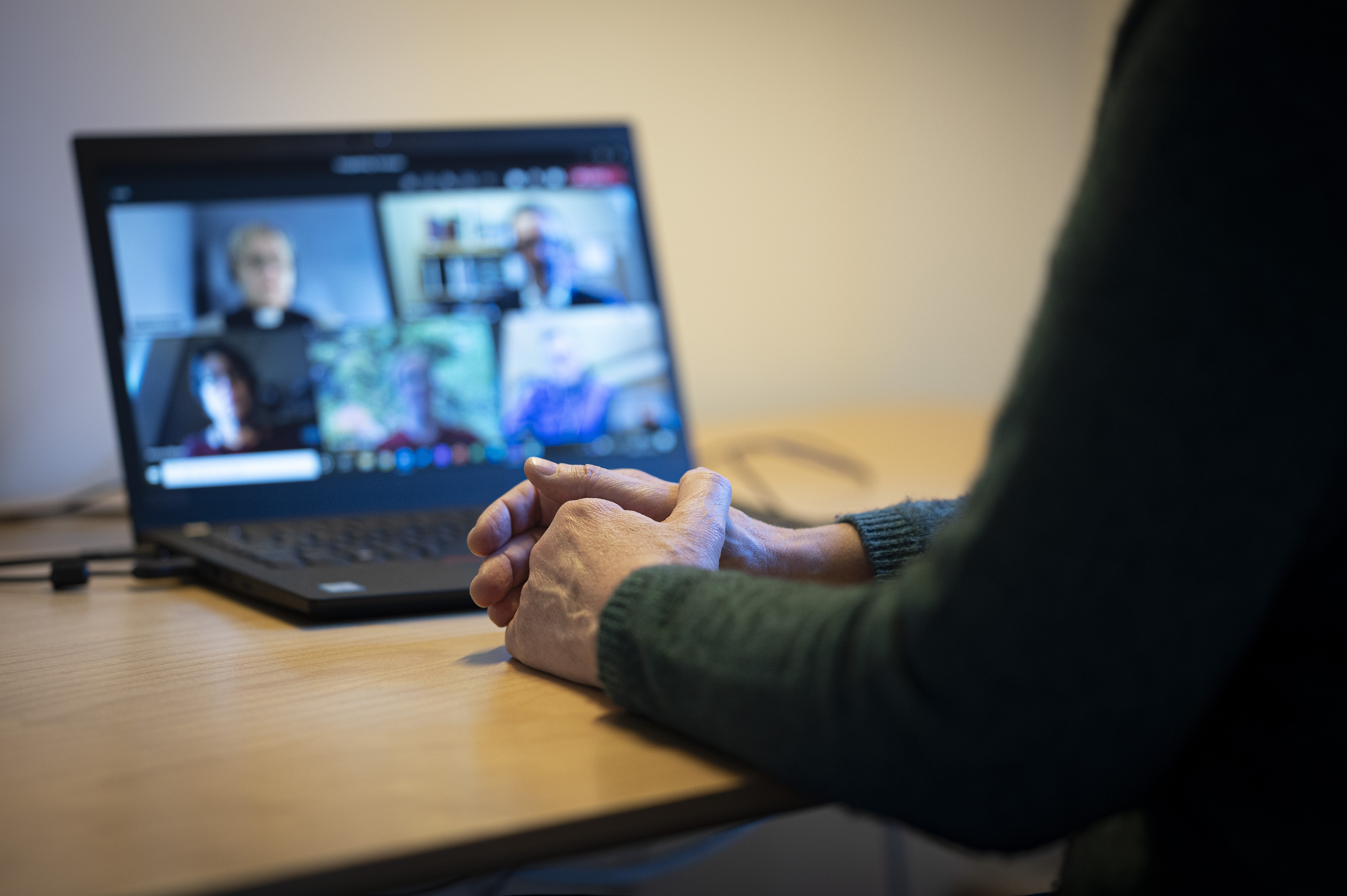 En person sitter vid ett skrivbord och har ett digitalt möte i datorn med några andra.