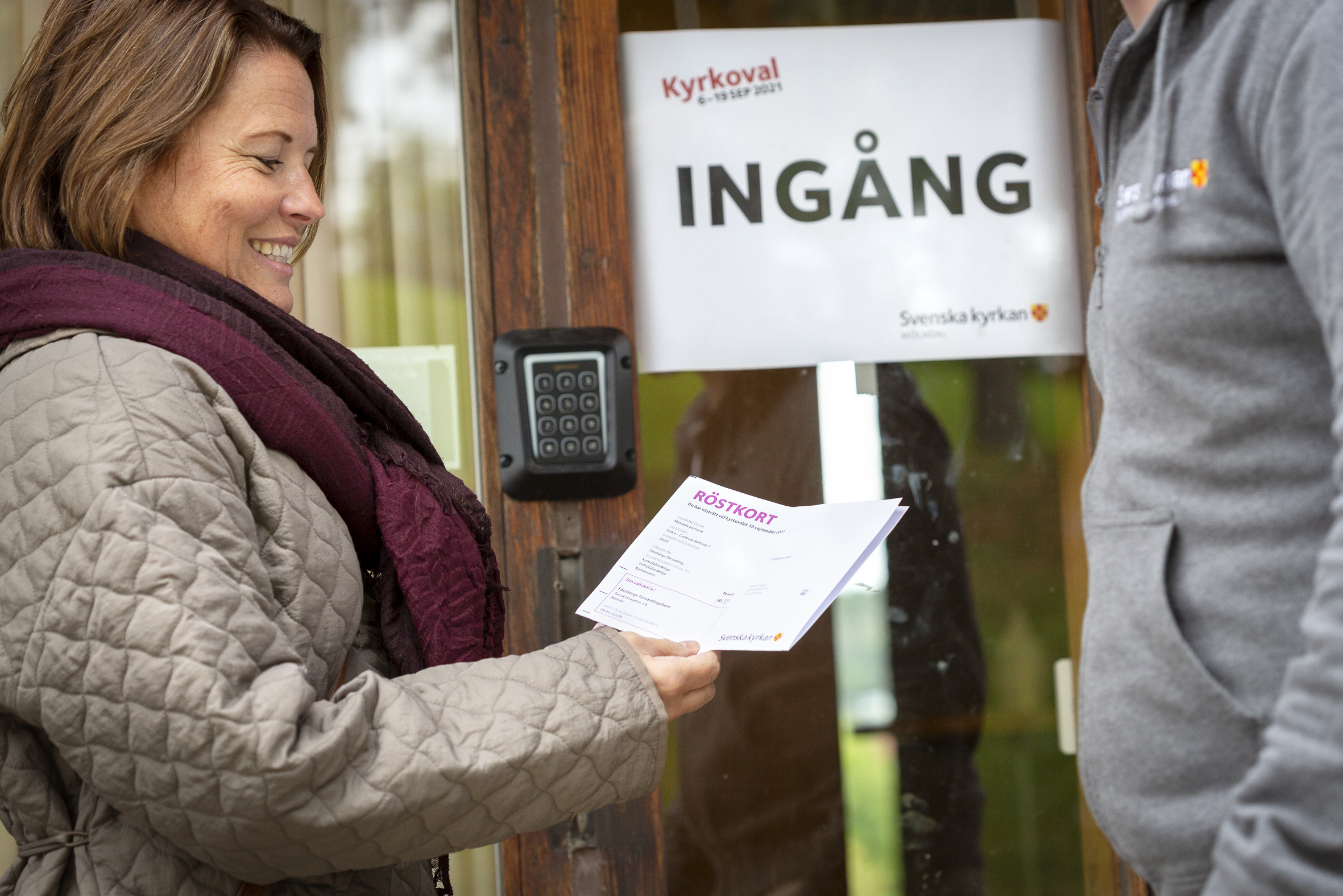 En kvinna visar upp sitt röstkort utanför ingången till en vallokal för Kyrkovalet.
