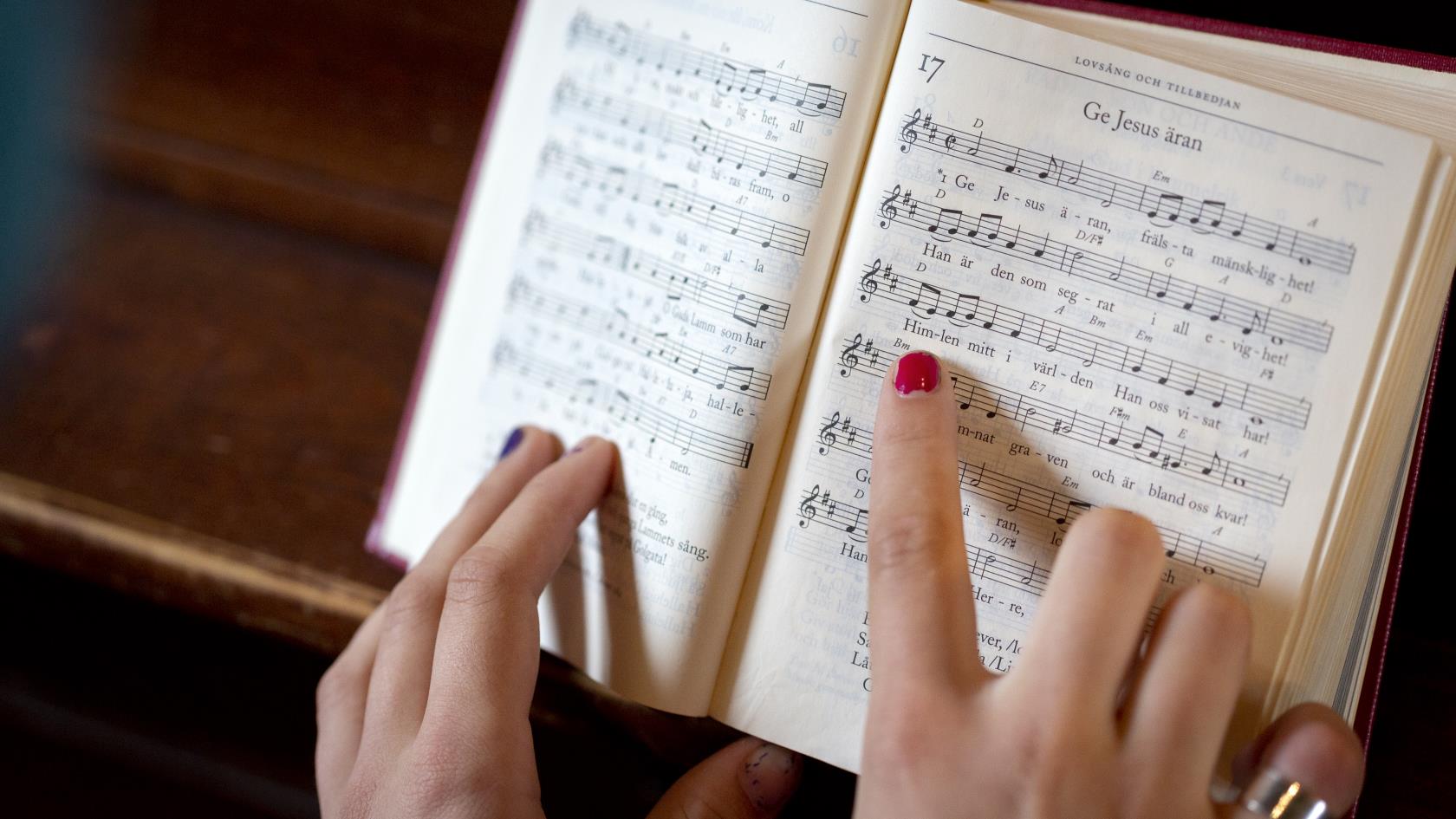 En person med målade naglar följer med sitt pekfinger melodin i en uppslagen psalmbok.