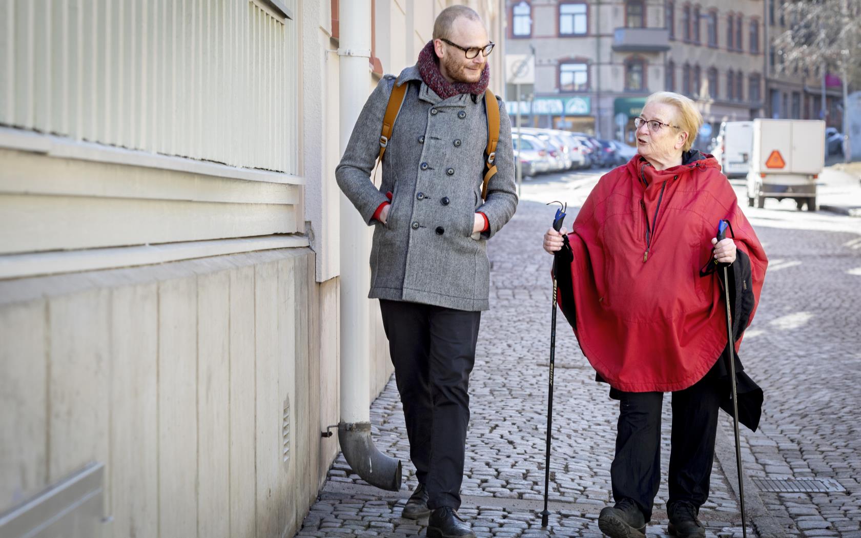 Än äldre kvinna med stavar är ute och promenerar på stan tillsammans med en ung man.