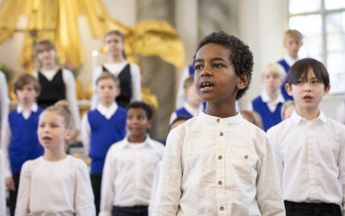 Medlemmar i en barnkör står och sjunger i en kyrka. En pojke står framför de andra och sjunger.