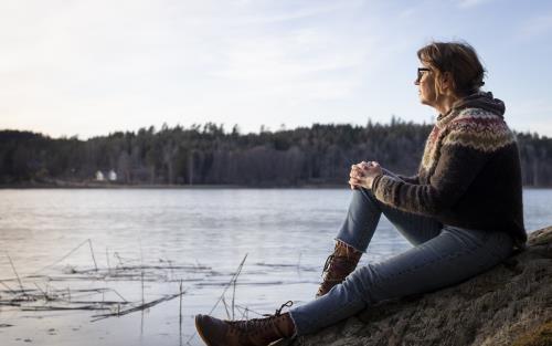 En kvinna sitter på en klippa och tittar ut över vattnet.