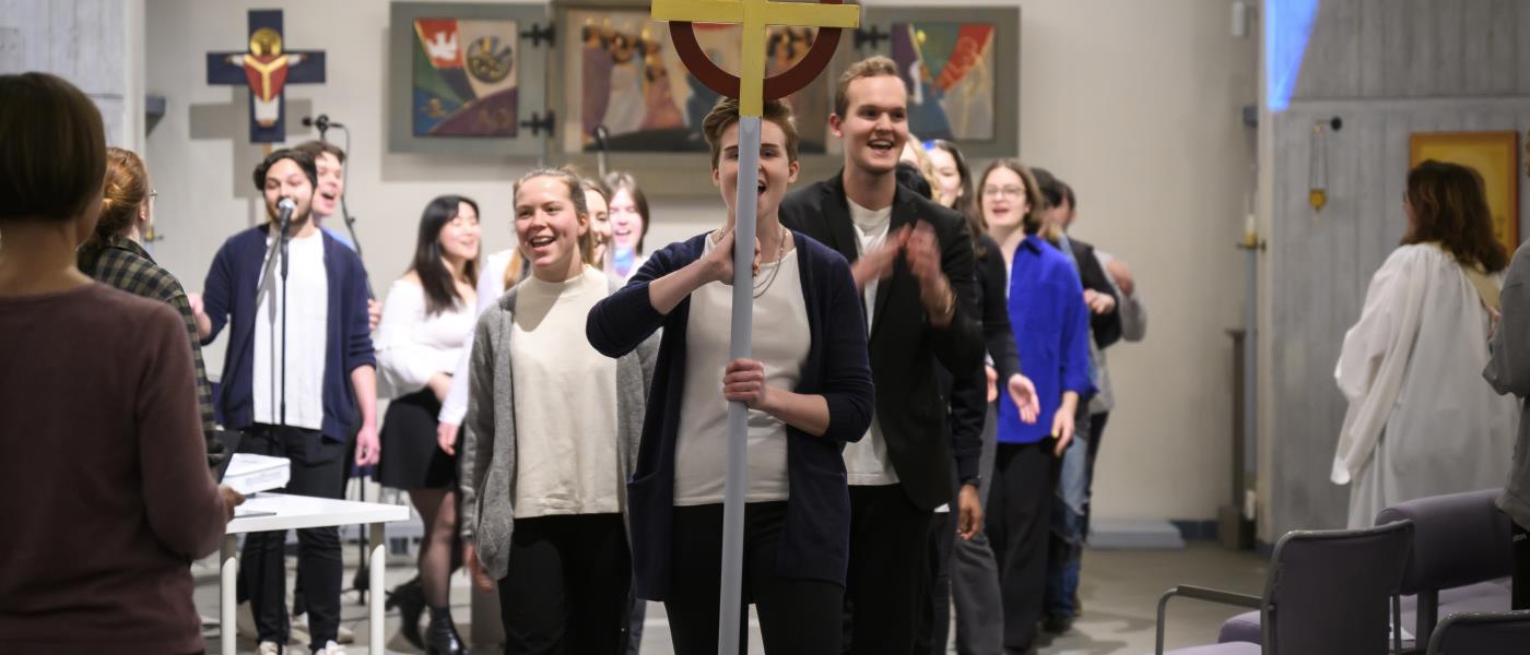 En ungdomskör går i procession genom en kyrka.