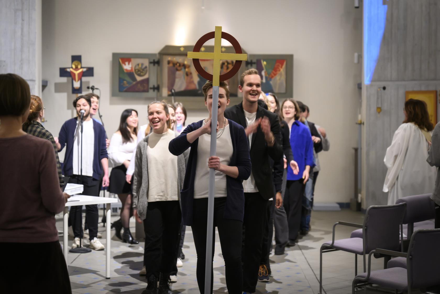 En ungdomskör går i procession genom en kyrka.