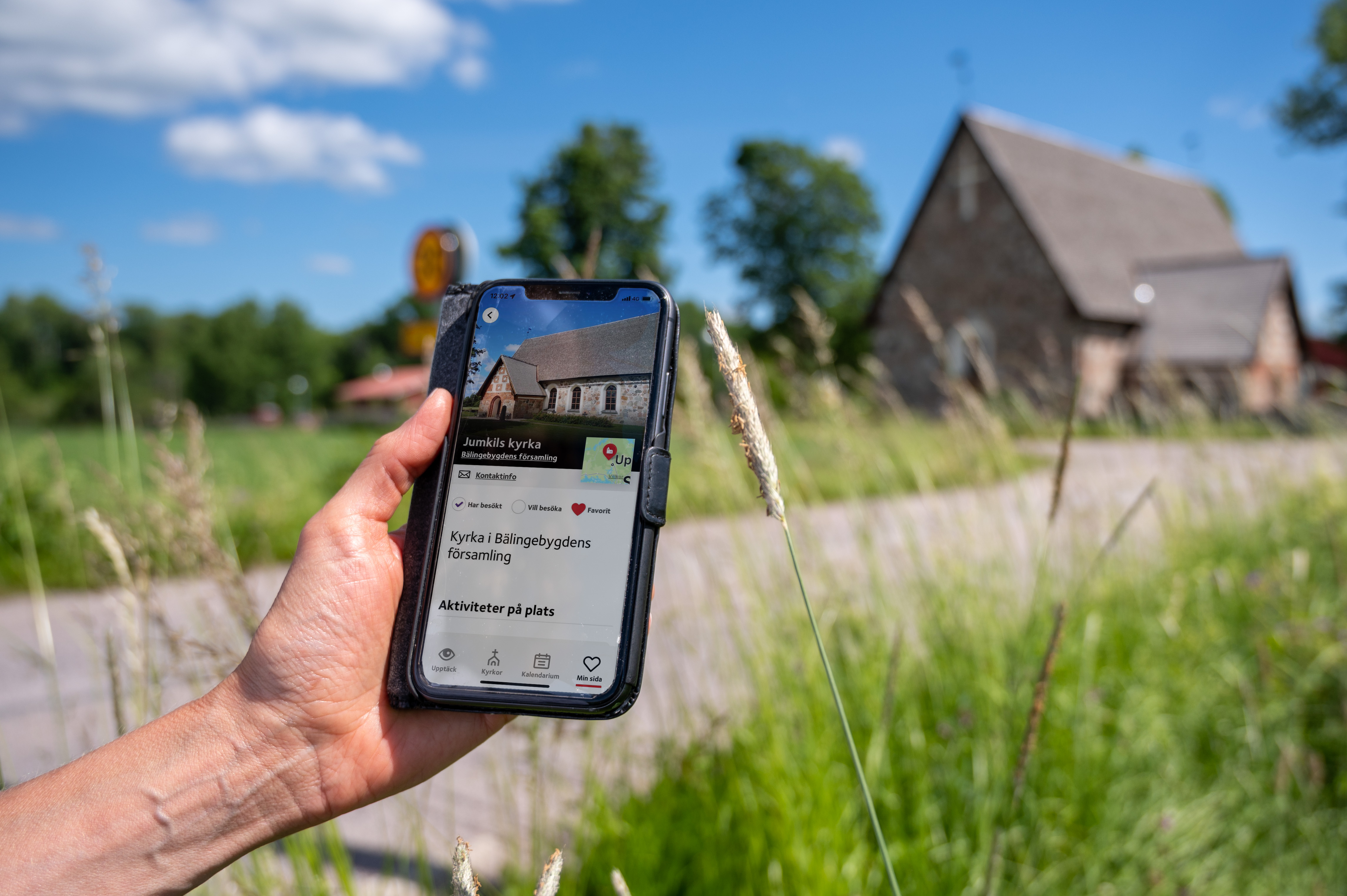 En person som kommit fram till en gammal kyrka håller en mobiltelefon i handen. På skärmen visas kyrkans namn och position på en karta.