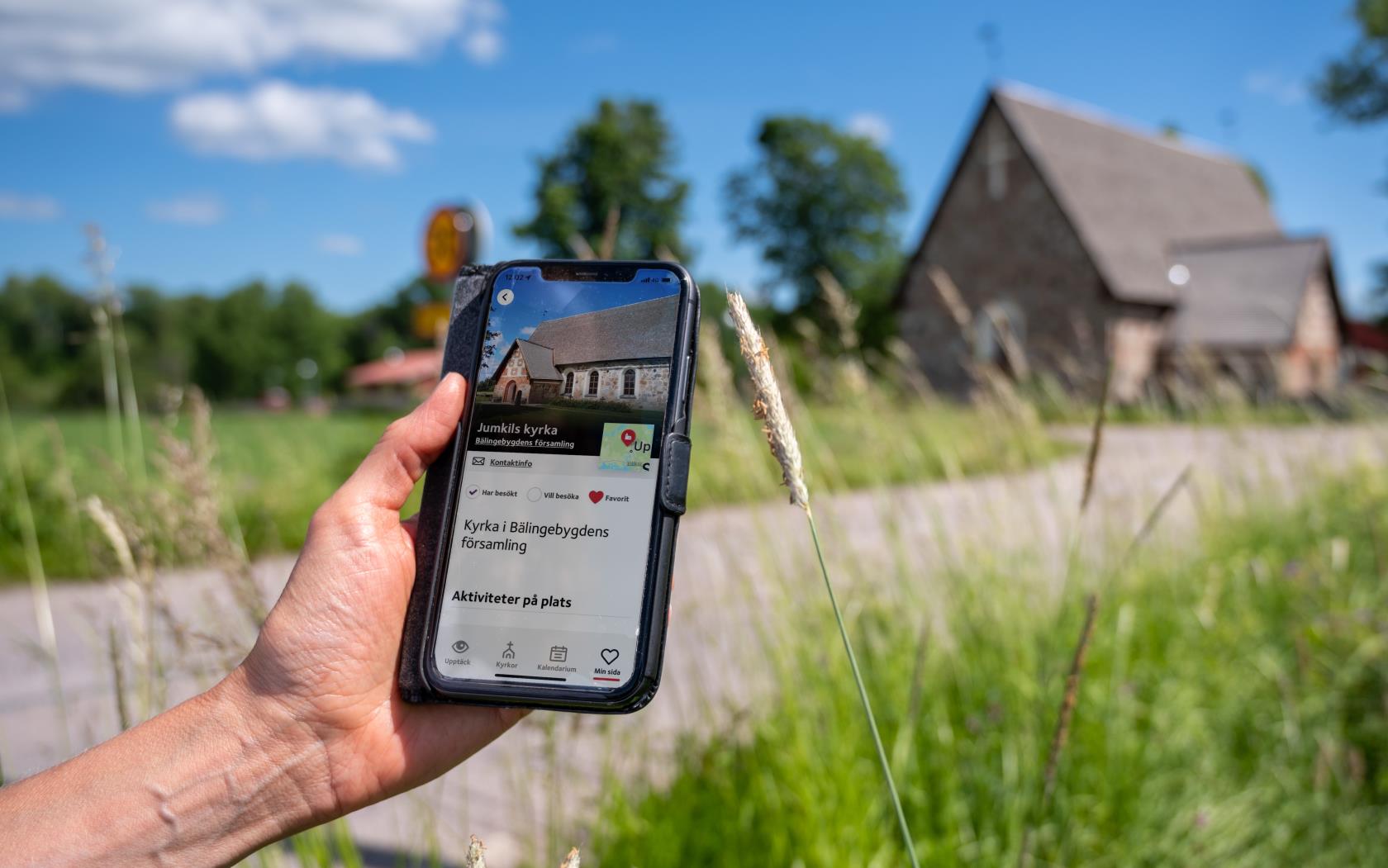 En person som kommit fram till en gammal kyrka håller en mobiltelefon i handen. På skärmen visas kyrkans namn och position på en karta.